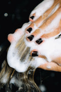 Close-up of hands massaging Decibel thickening shampoo lather through wet hair.